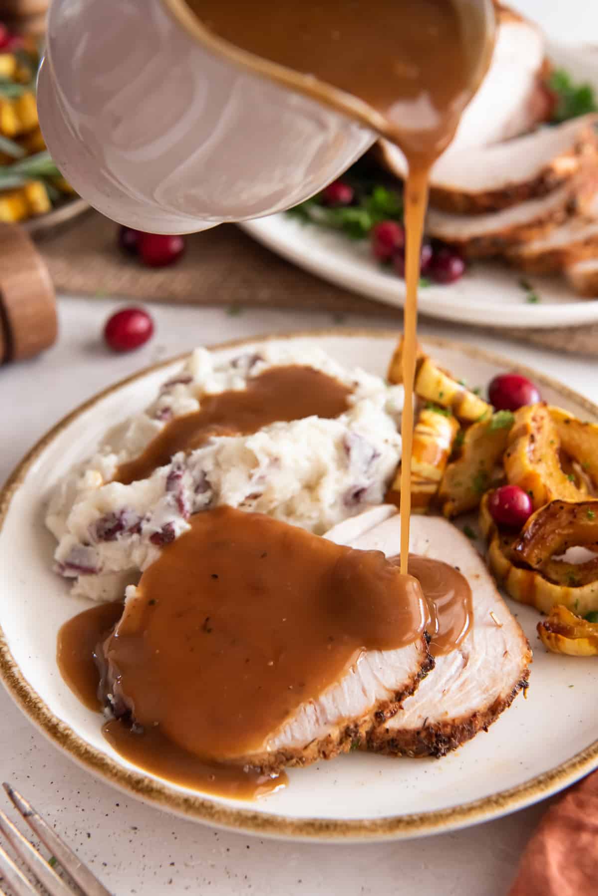 Gravy pouring on to slices of turkey breast on a white plate with mashed potatoes.