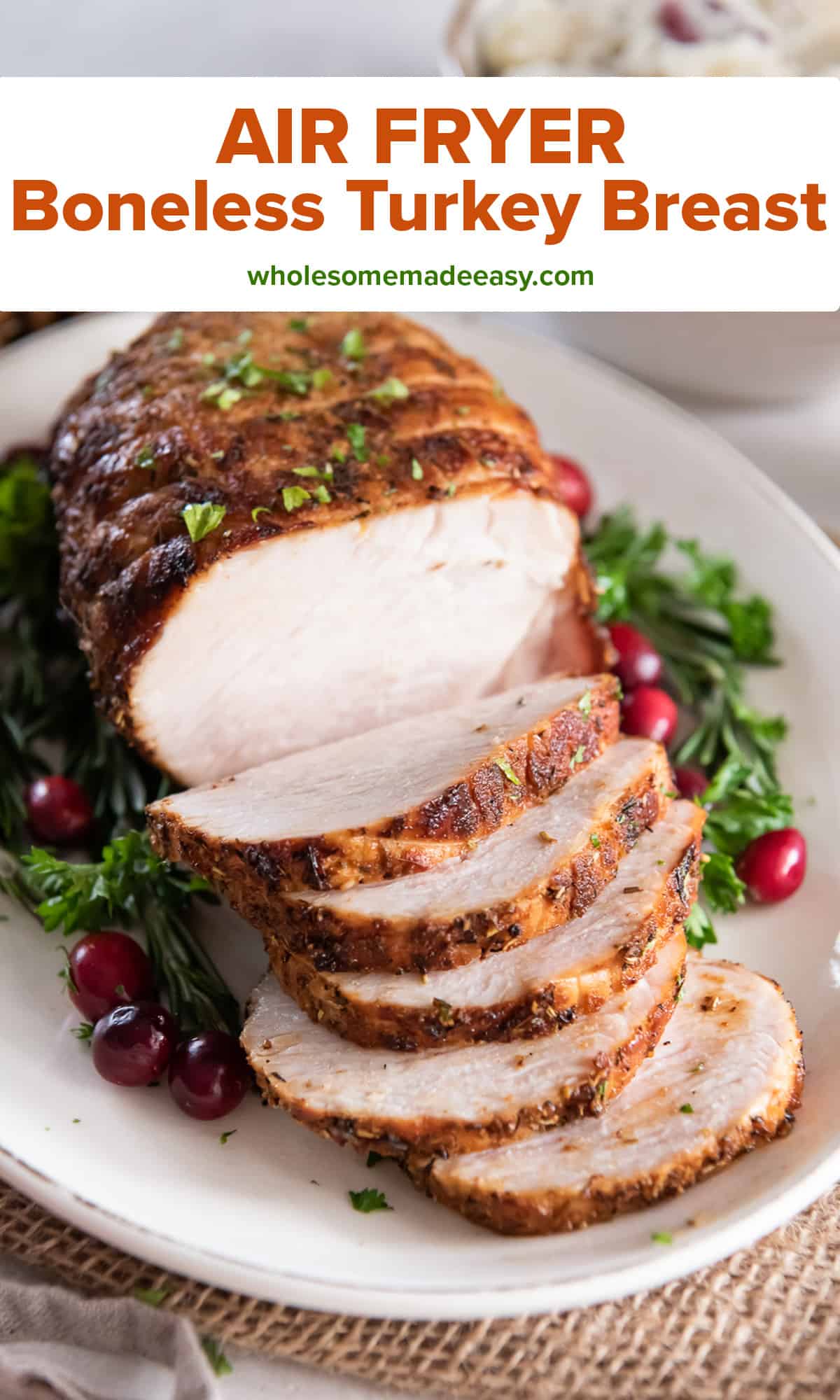 A sliced boneless turkey breast a white platter decorated with fresh herbs and cranberries with text.