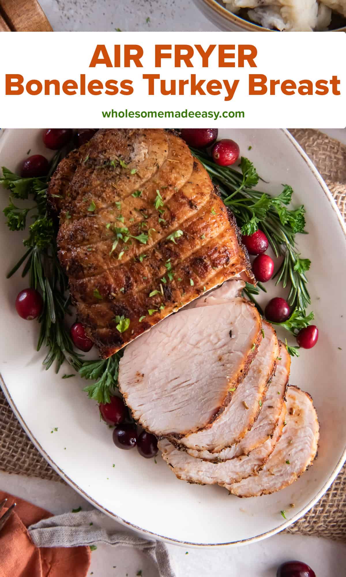 A sliced boneless turkey breast a white platter decorated with fresh herbs and cranberries with text.