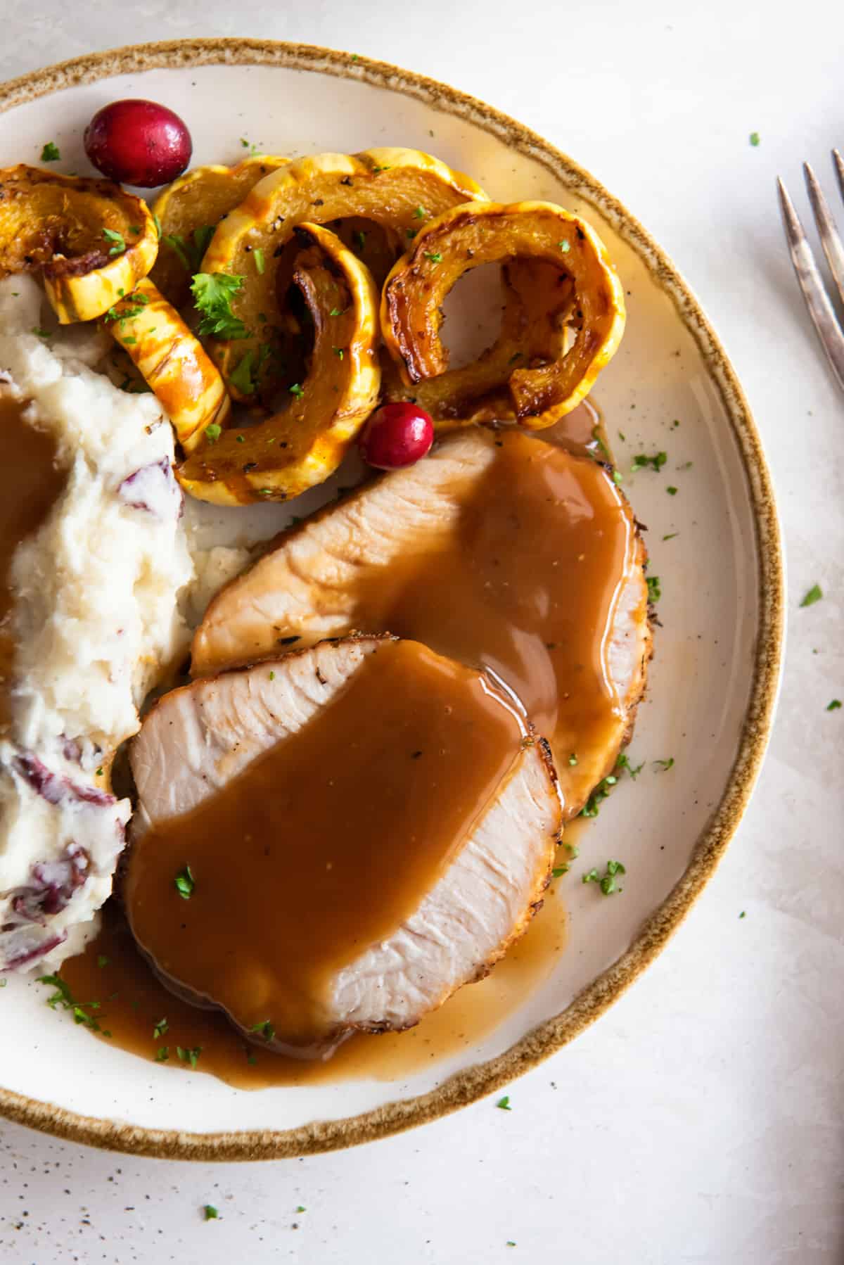 A top down shot of sliced turkey with gravy on a plate with potatoes and squash.