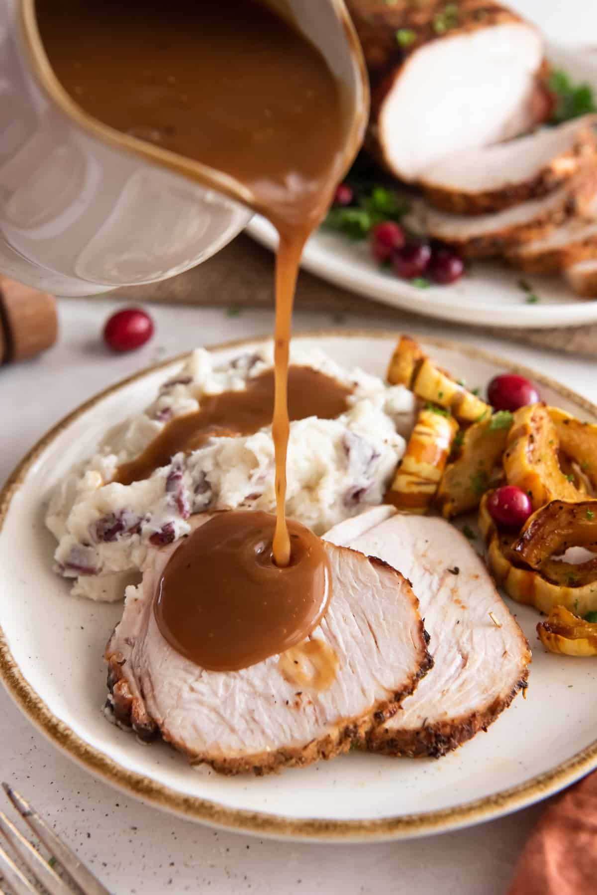 Gravy pouring from a gravy boat on to sliced turkey on a plate.