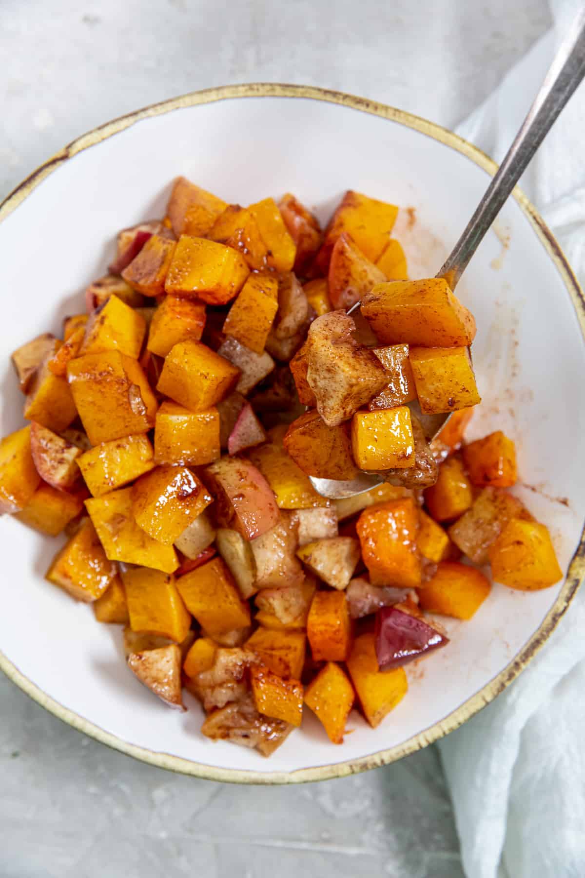 A spoon lifts roasted butternut squash and apples from a white bowl.