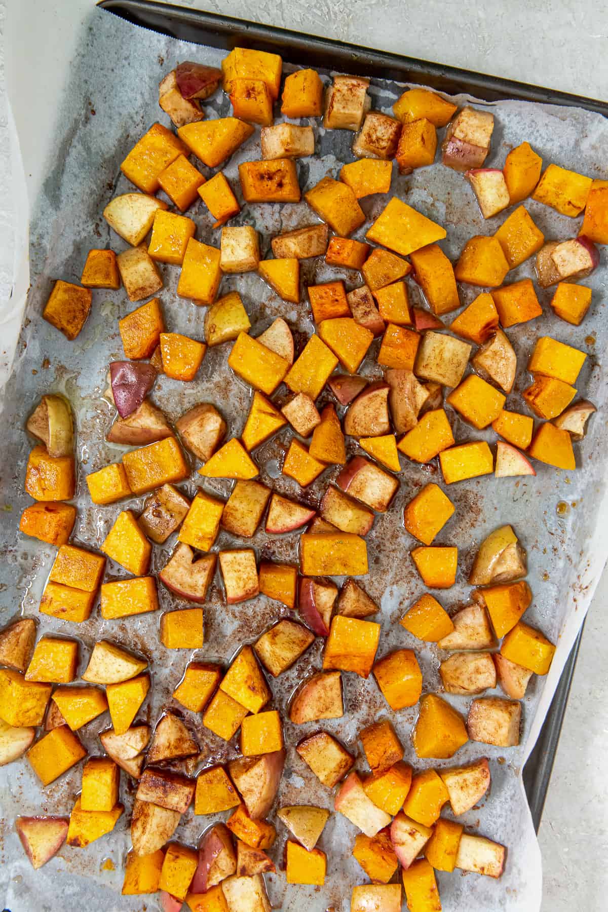 A top down shot of roasted butternut squash and apples on a parchment paper lined baking sheet.