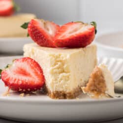 A slice of cheesecake on a white plate with a bite missing topped with strawberries.