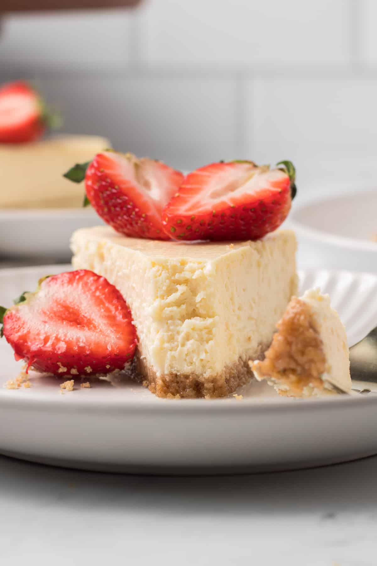 A slice of cheesecake on a white plate with a bite missing topped with strawberries.