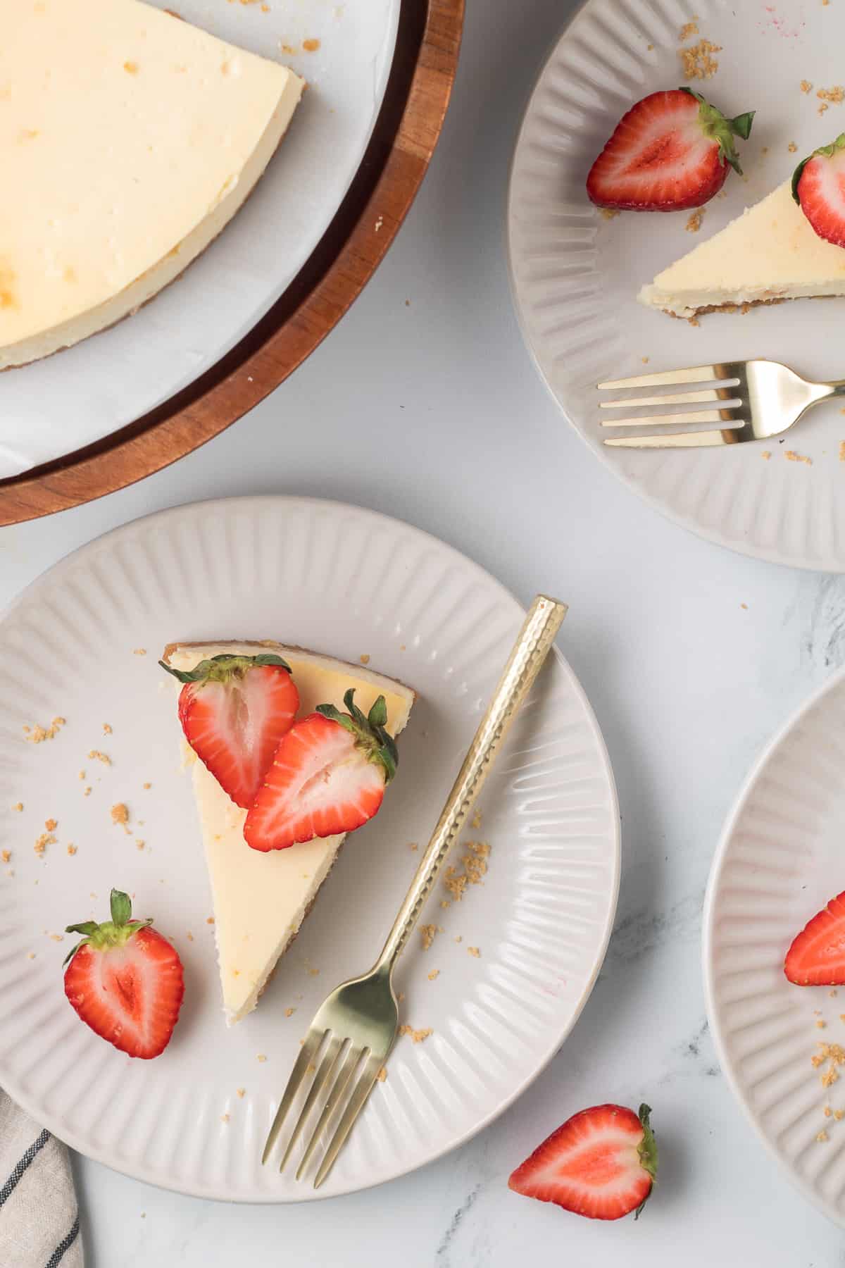 A top down shot of slices of cheesecake topped with strawberries on white plates with forks.