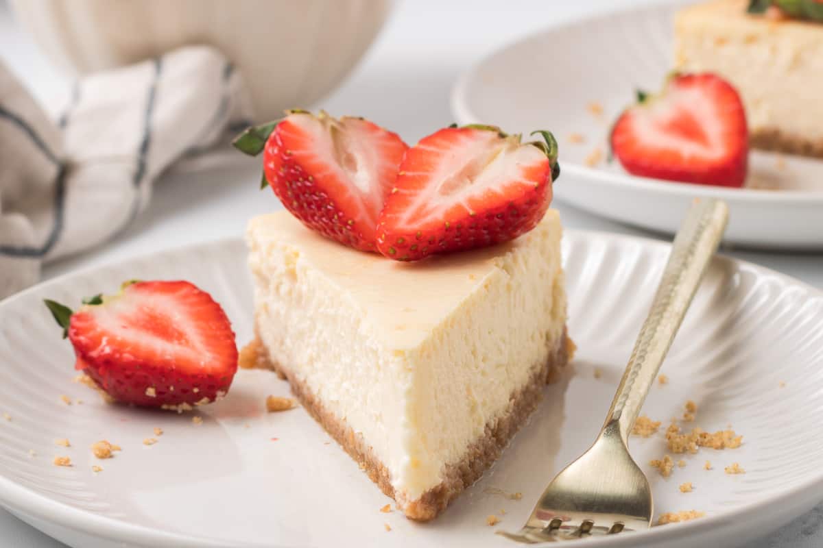 A close up of a slice of cheesecake topped with strawberries on a white plate with a fork.