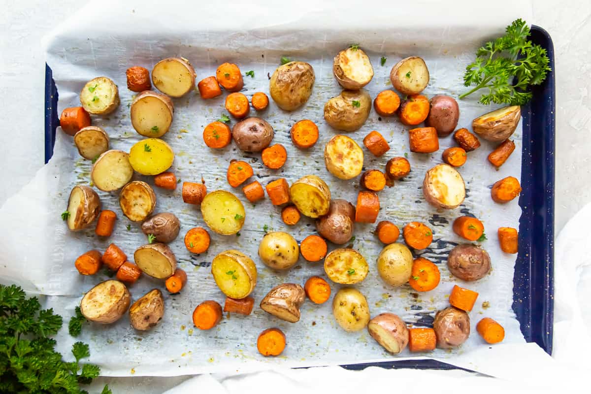 Chunks of roasted carrots and potatoes on a parchment paper lined baking sheet.