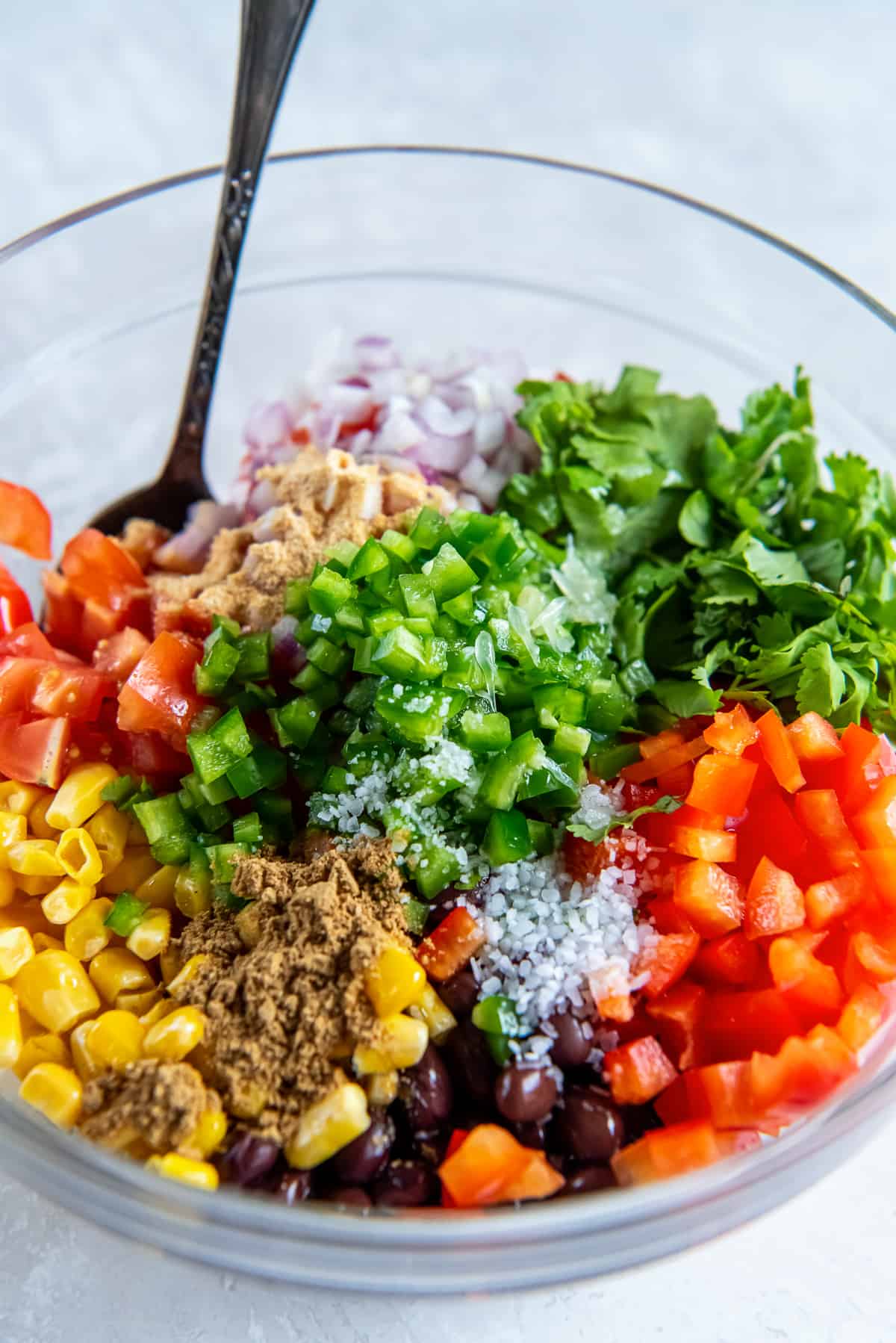 Corn, black beans, bell pepper, tomato and other ingredients in a large mixing bowl with a spoon.