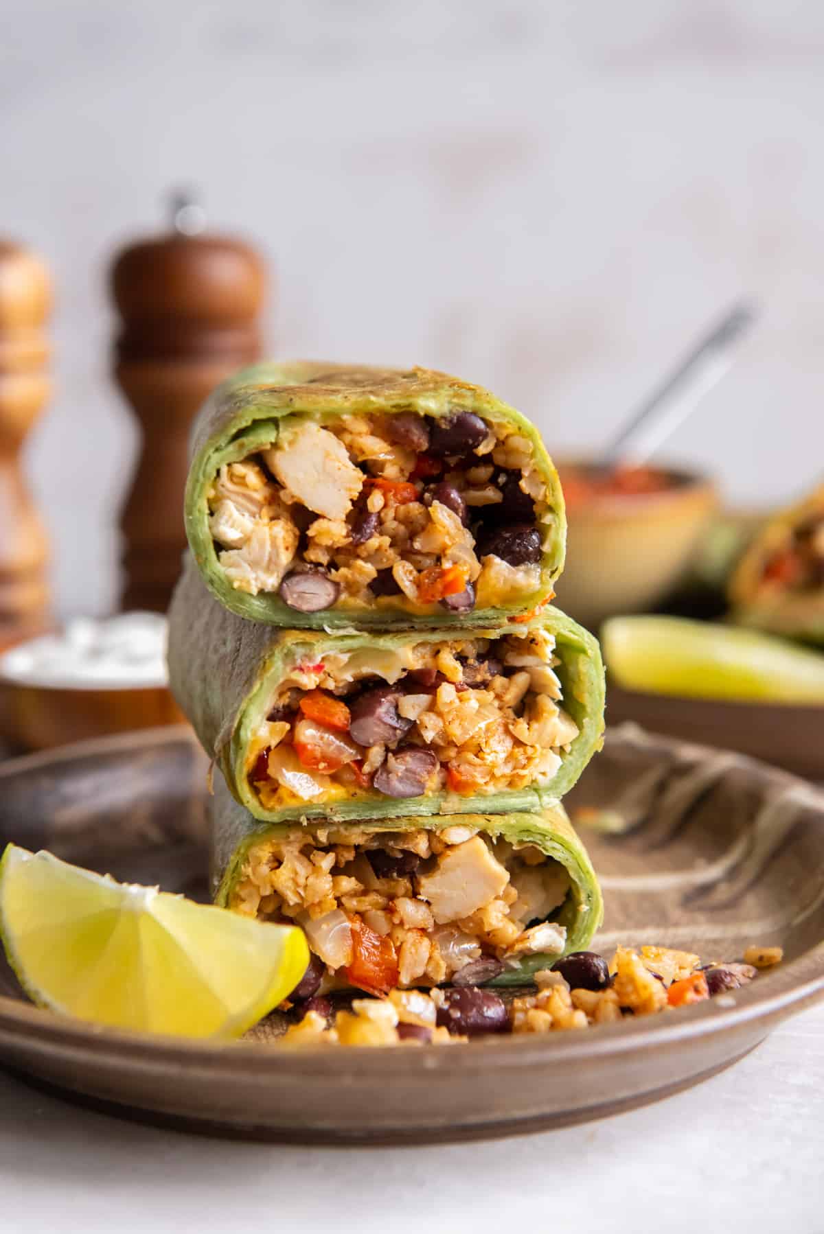 A stack of halved burritos in green tortillas revealing the filling of rice, black beans, red bell peppers, and chicken.