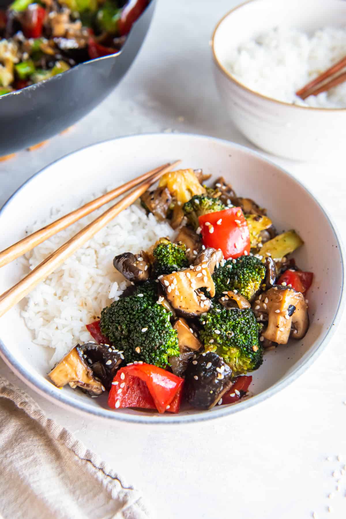 Broccoli mushroom stir fry in a bowl with white rice and chopsticks.