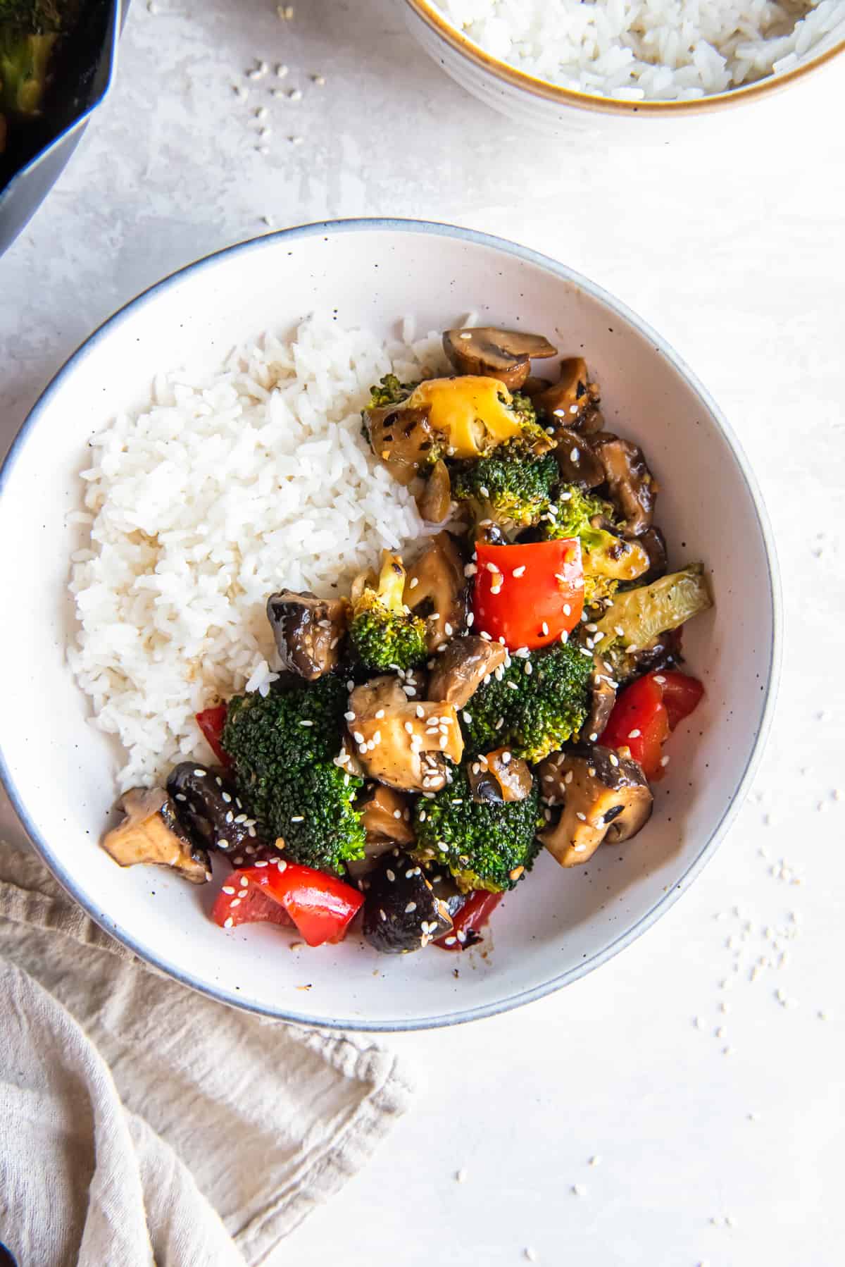 A top down shot of broccoli mushroom stir fry with white rice in a bowl.