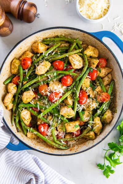 A top down shot of chicken with pesto and vegetables in a skillet.