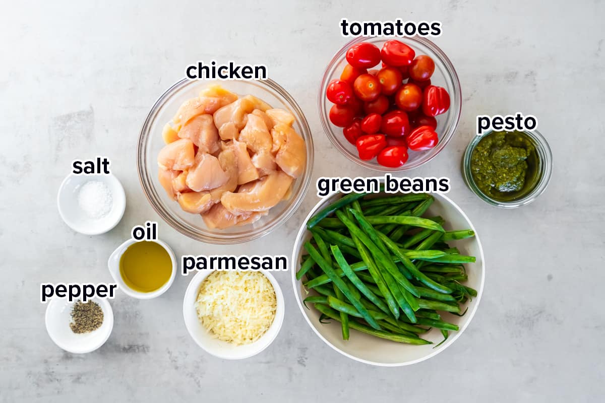 Chunks of chicken, pesto, green beans, tomatoes and other ingredients in bowls with text.
