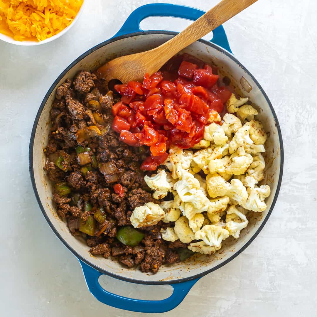 Cooked ground beef, cauliflower, and tomatoes in a skillet.