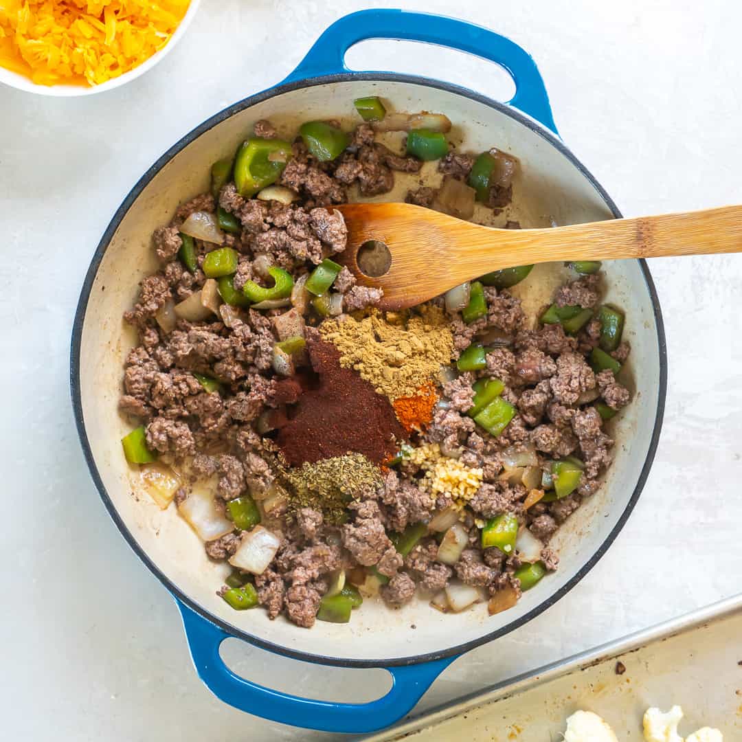 A top down shot of cooked ground beef with seasoning, green bell pepper, and onion.