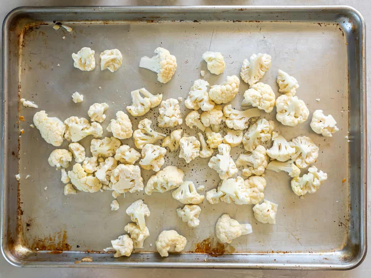 Cauliflower florets coated with oil and seasoning on a baking sheet.