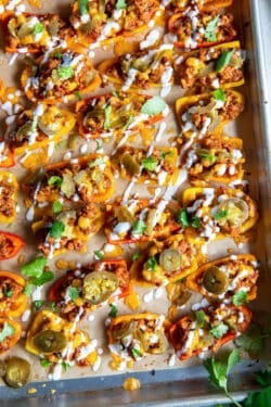 A top down shot of stuffed mini bell peppers on a baking sheet topped with sour cream, jalapenos, and cilantro.