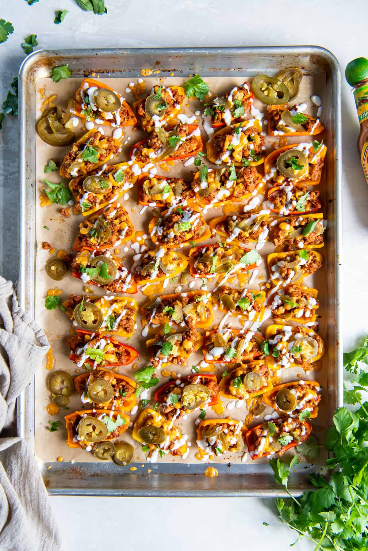 A top down shot of mini bell pepper nachos topped with sour cream, jalapenos, and cilantro on baking sheet.