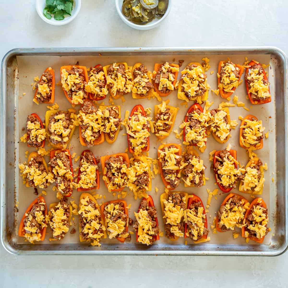 Sliced mini bell peppers on a baking sheet stuffed with a meat filling.