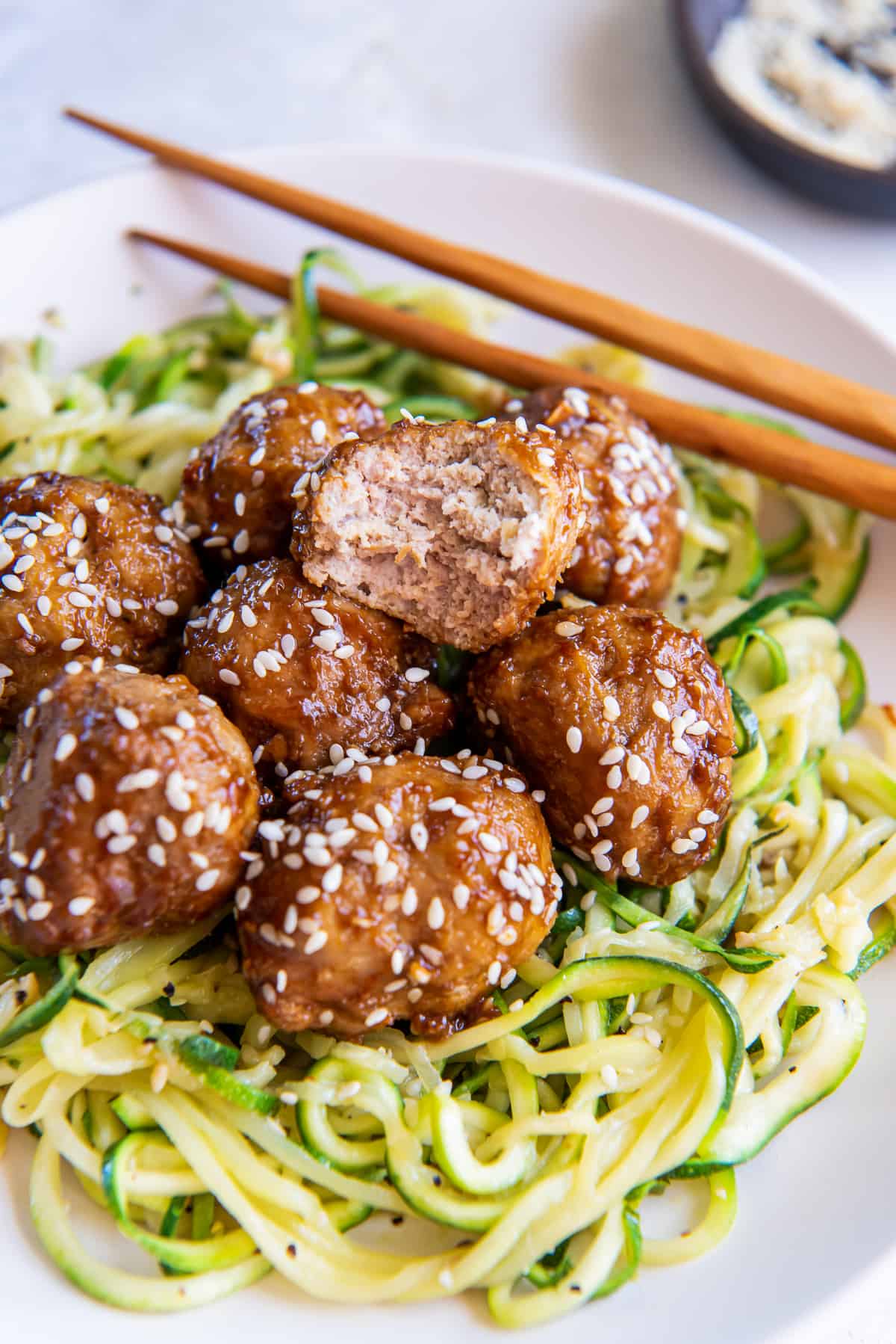 A pile of Asian meatballs over zucchini noodles with a bite missing from the meatball on top.