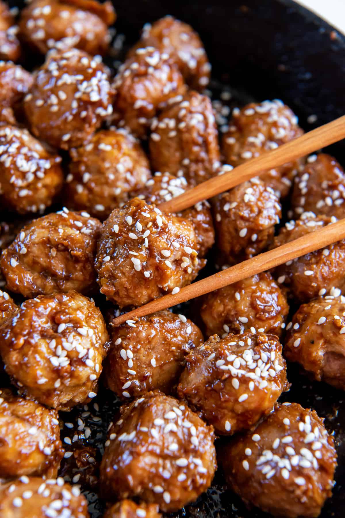 A closeup of chopsticks holding a meatball in a skillet.