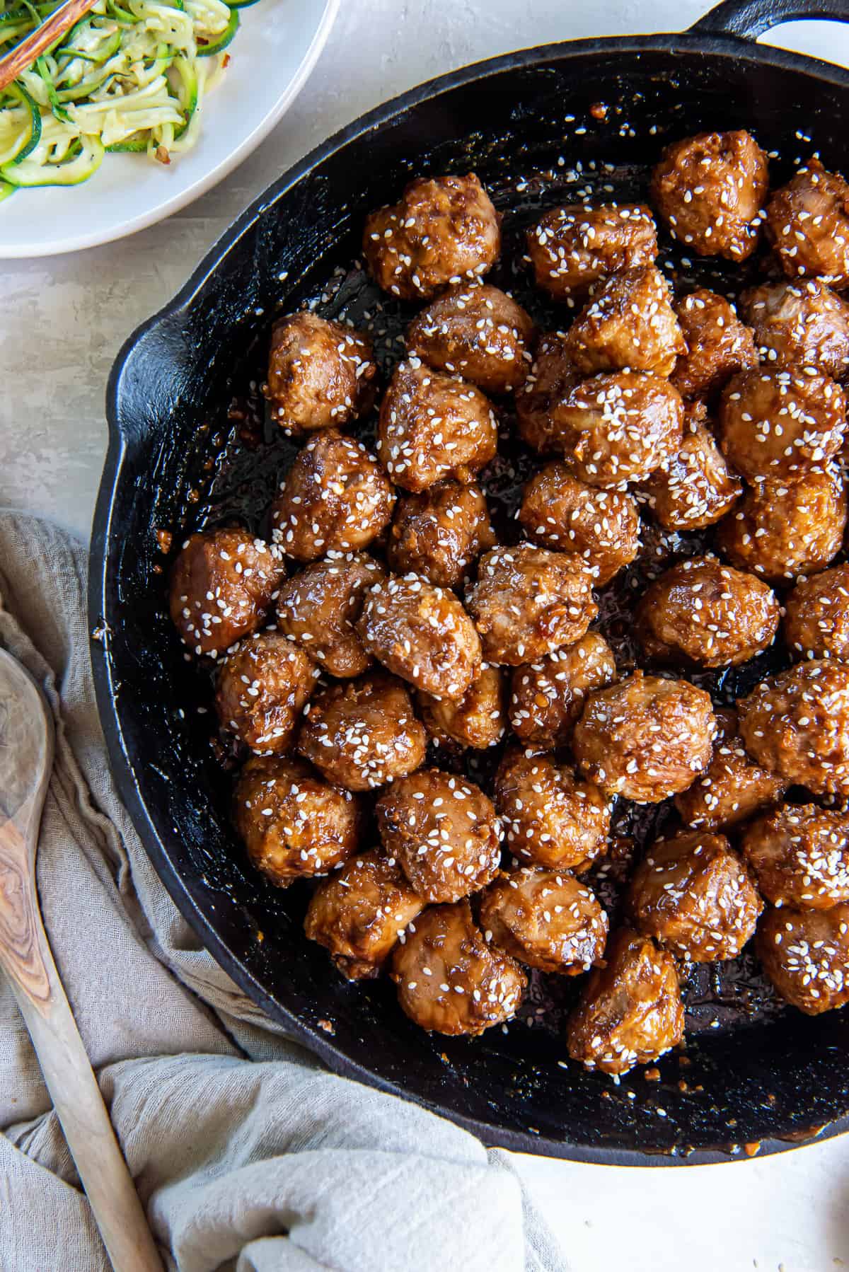 A top down shot of Asian meatballs topped with sesame seeds in a cast iron skillet.