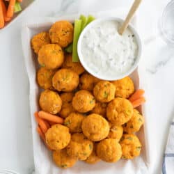 A top down shot of a platter of buffalo chicken bites with a small bowl of blue cheese dip with a platter of veggies next to it.
