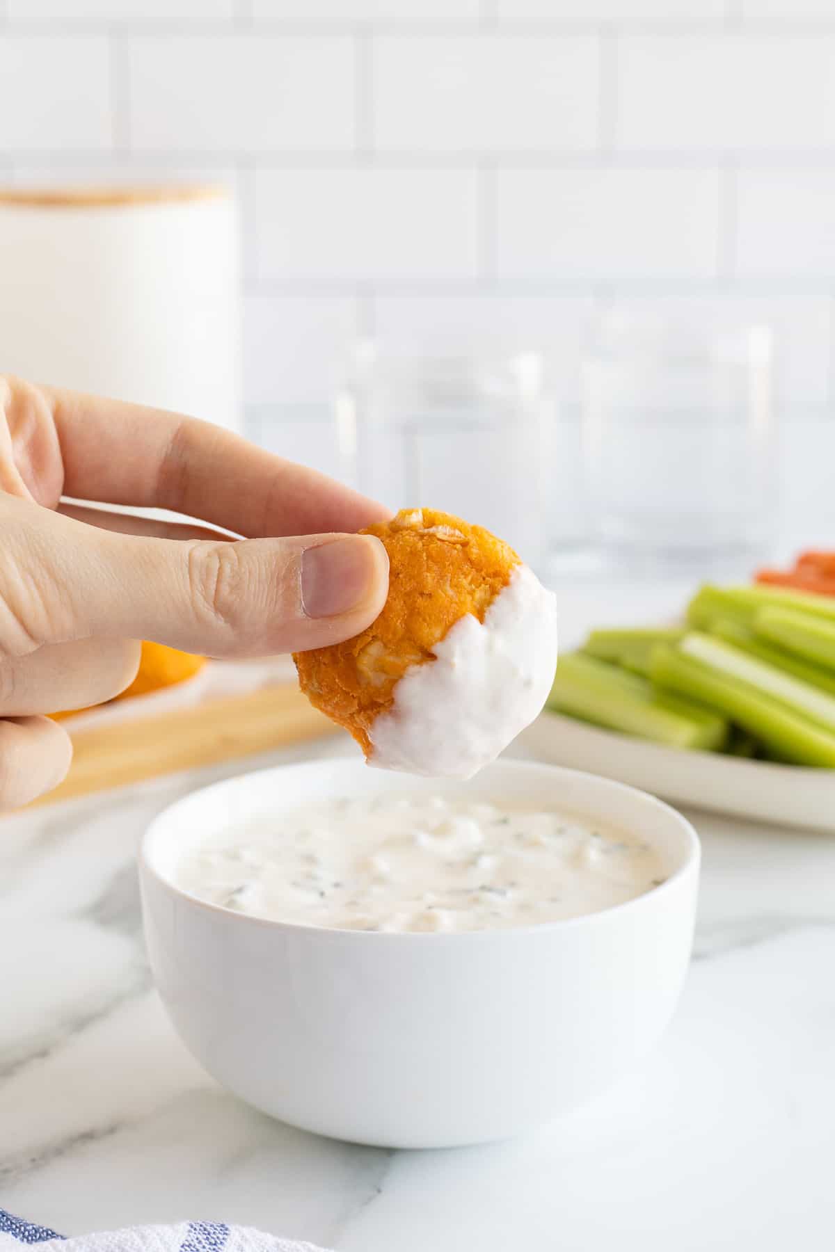 A hand holding a buffalo chicken bite that has been dipped in blue cheese sauce.