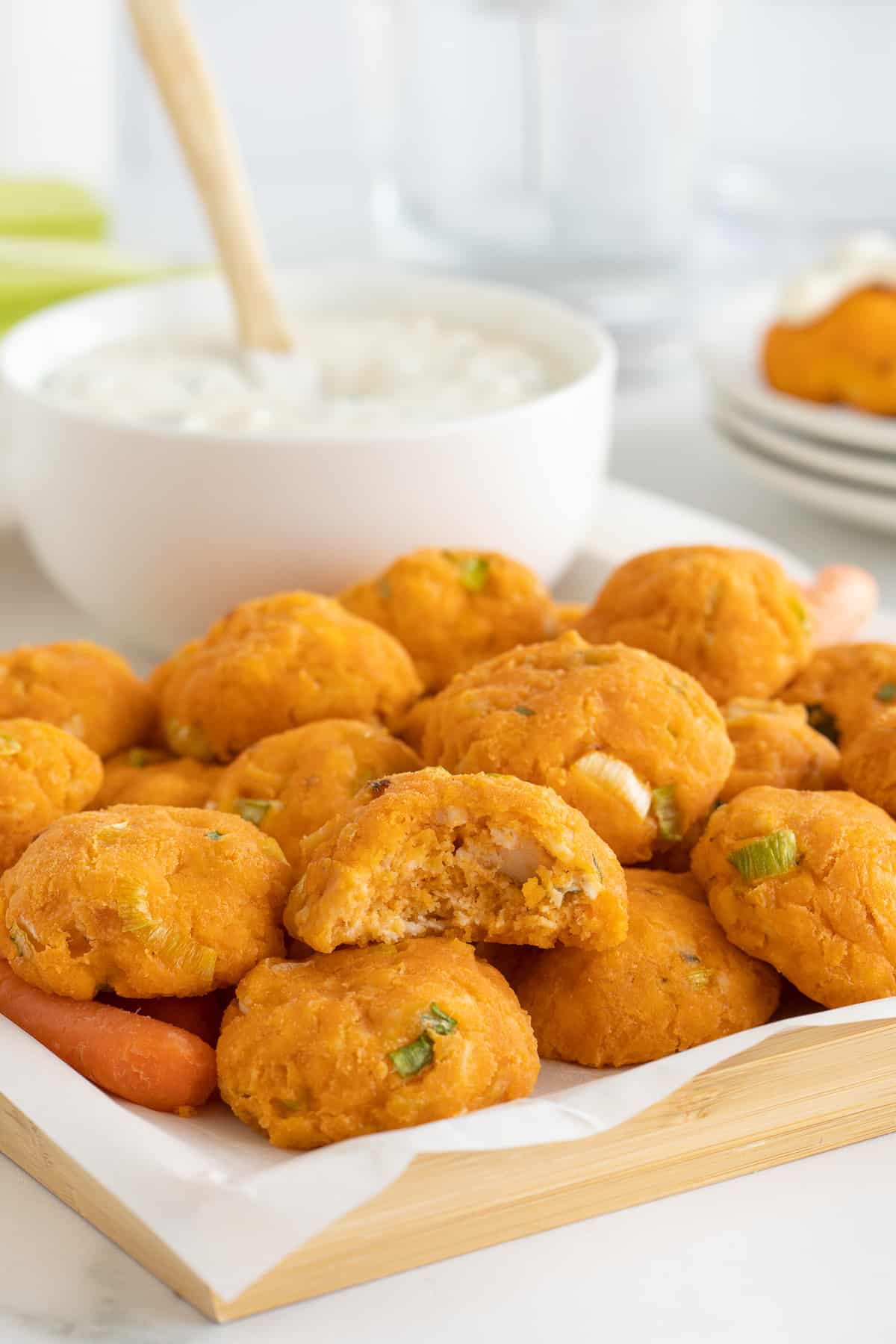 A pile of buffalo chicken bites on a platter with a bite missing from the one on top.