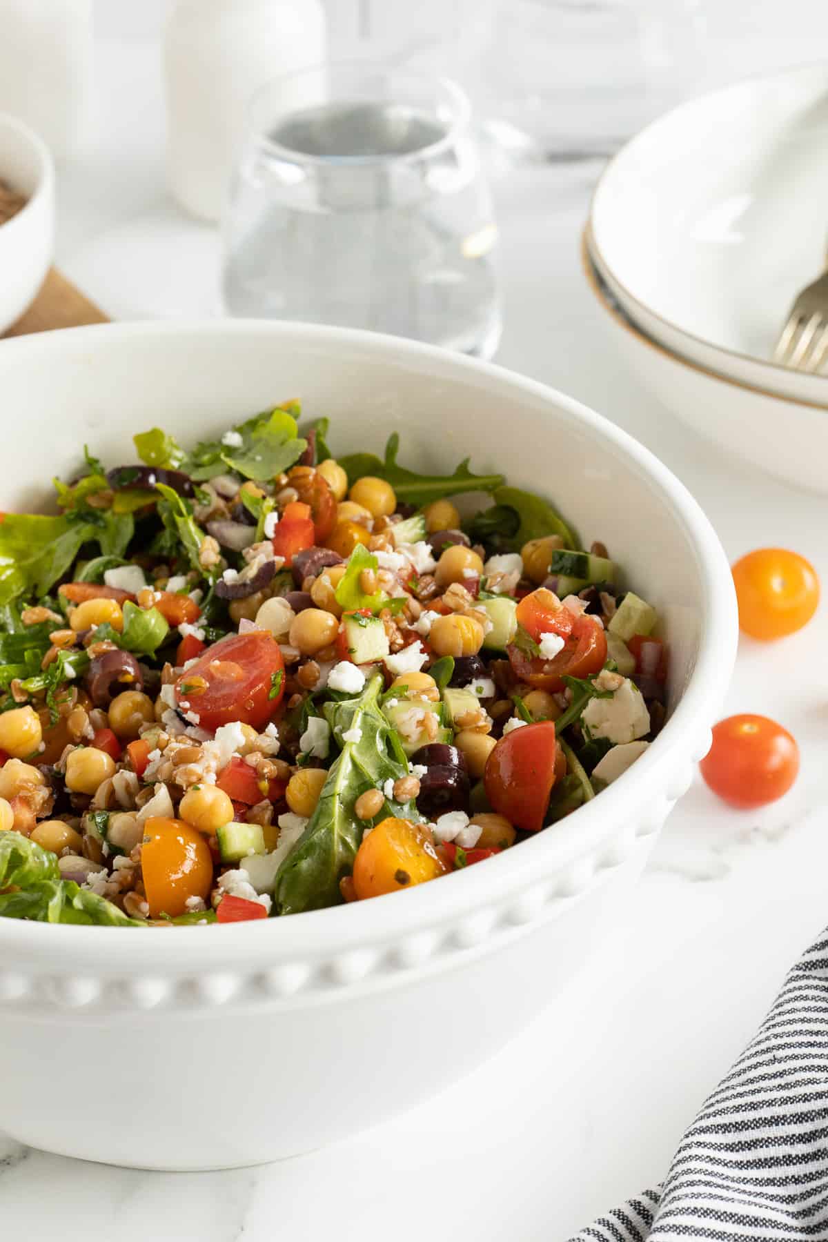 A side view of a Greek salad with farro in a large white serving bowl.