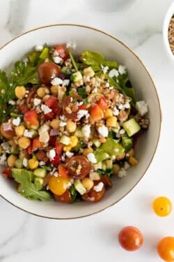 A top down shot of Greek farro salad in a salad bowl with cherry tomatoes scattered around it.