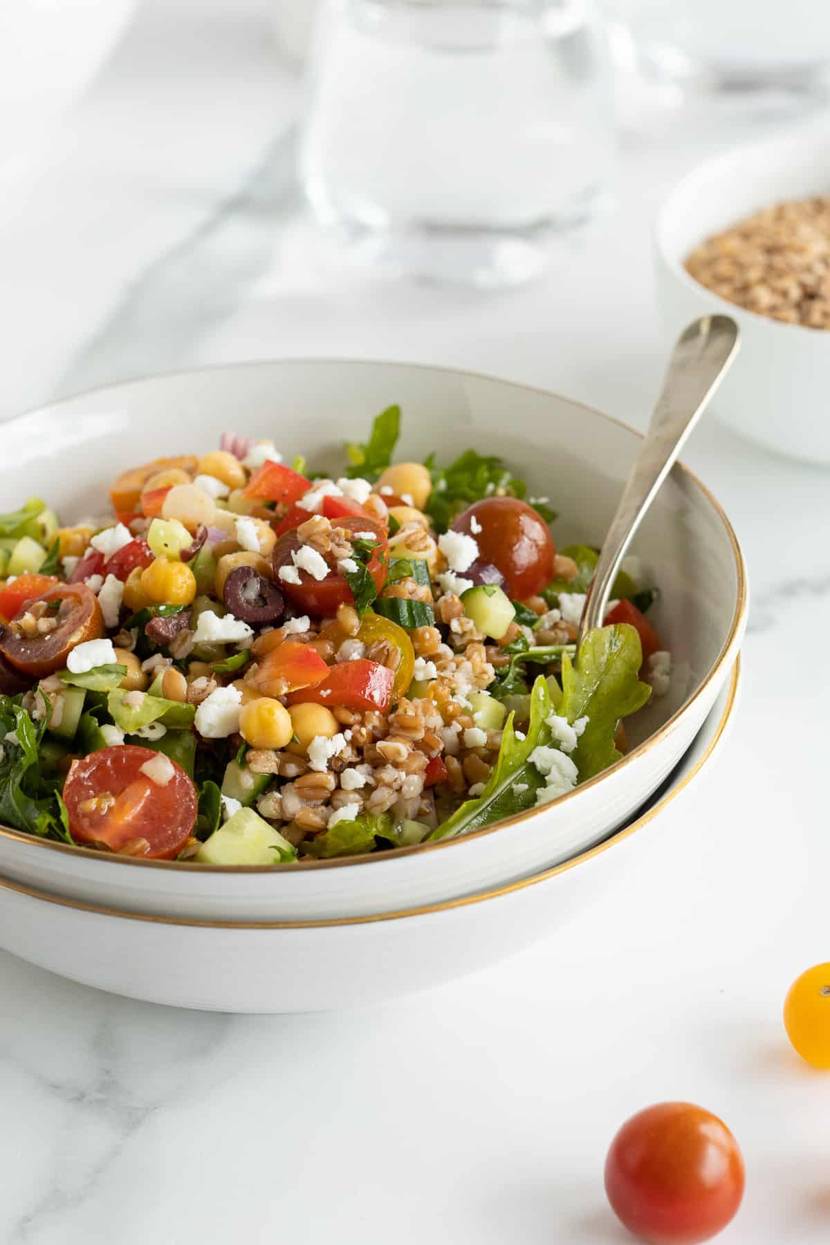 A side view of Greek farro salad in a white salad bowl with a fork stacked inside another bowl.