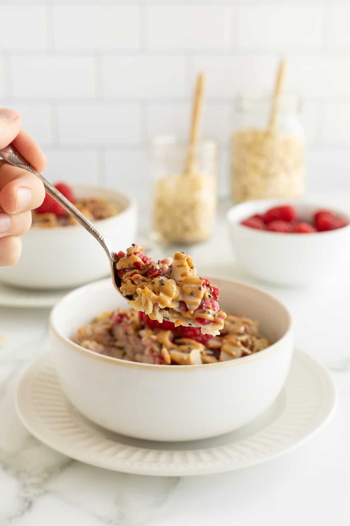 A spoon lifting a scoop of oatmeal with raspberries, peanut butter, and almonds.
