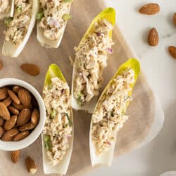 A top down shot of endive leaves stuffed with tuna salad on a cutting board with a small bowl of almonds.
