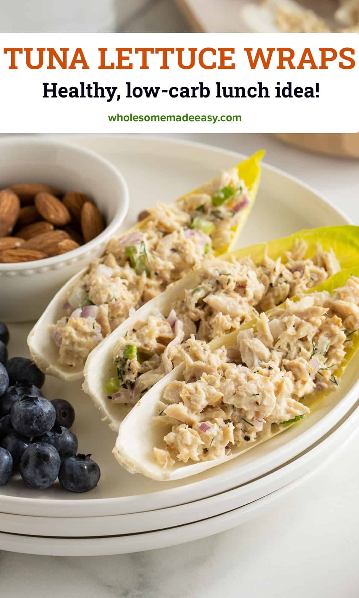 A side view of endive leaves stuffed with tuna salad to make tuna lettuce wraps on a white plate with blueberries and a small bowl of almonds.