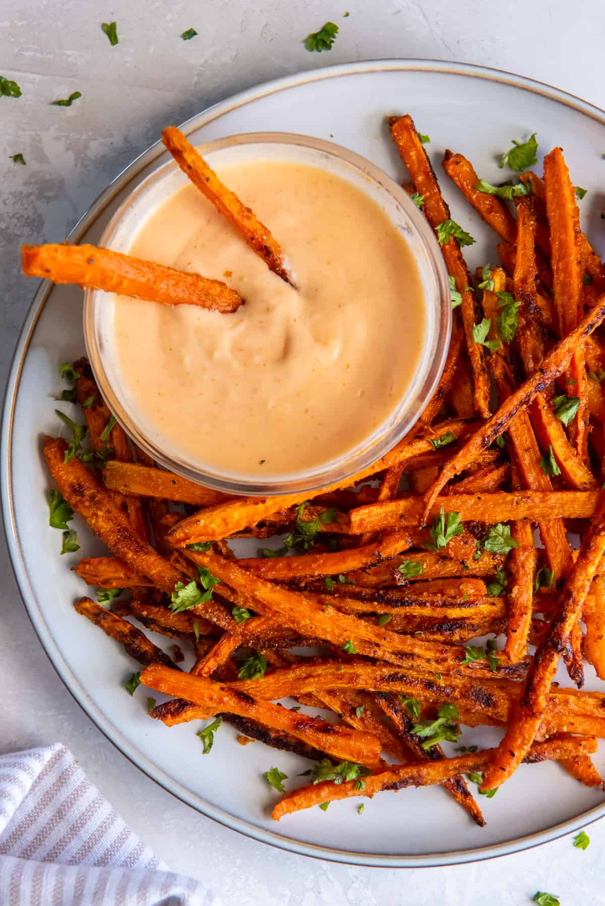 Two carrot fries resting in a bowl on sriacha dipping sauce on a white plate.