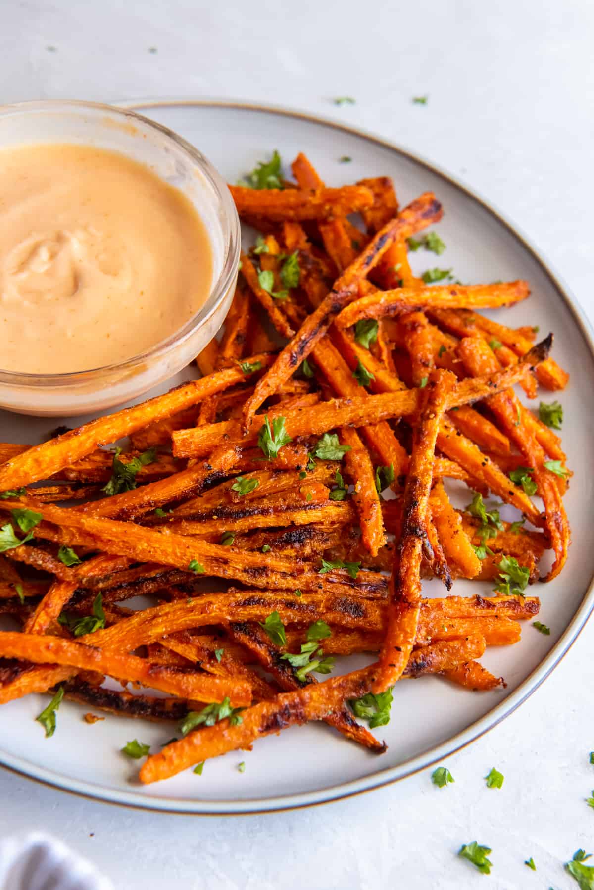 Carrot fries on a white plate with a small bowl of sriracha dipping sauce.