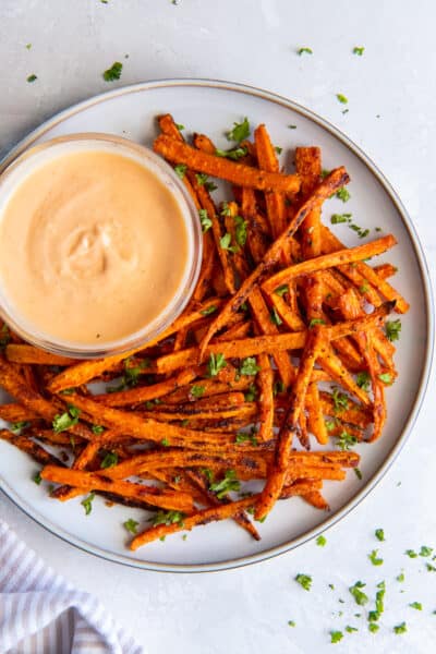 A top down shot of carrot fries on a plate with a small bowl of sriracha honey dipping sauce.