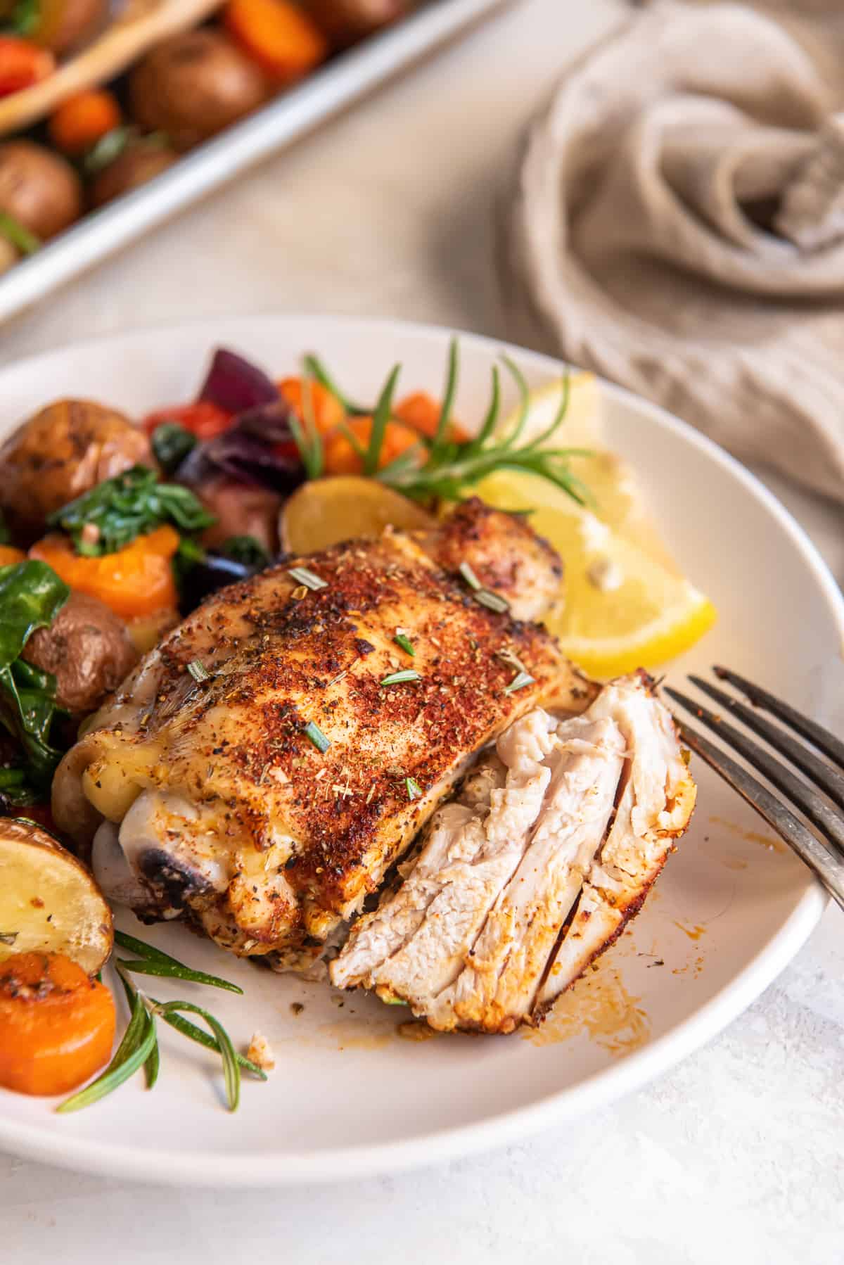 Sliced chicken thigh on a white plate with roasted vegetables.