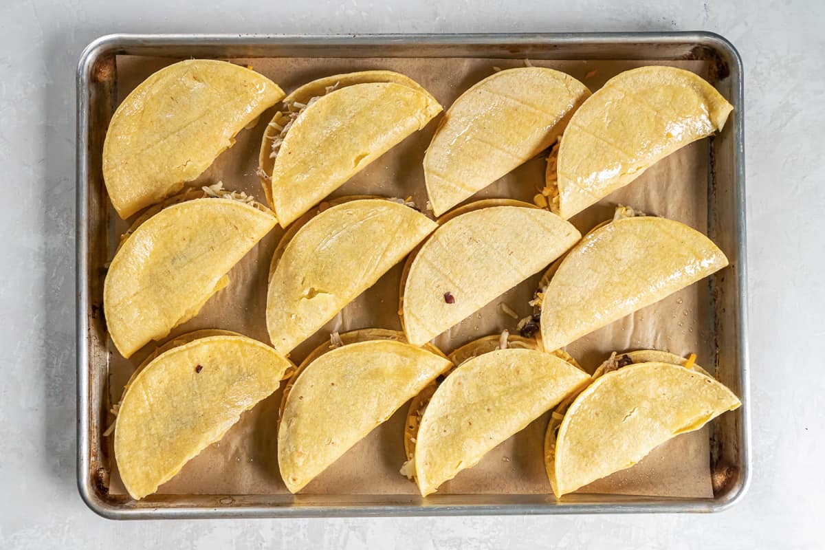 Chicken tacos on a baking sheet lined with parchment paper.