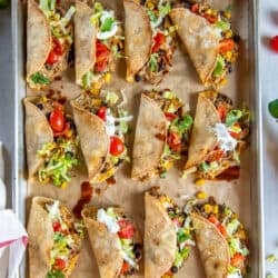 A sheet pan full of chicken tacos filled with lettuce, tomatoes, and sour cream.
