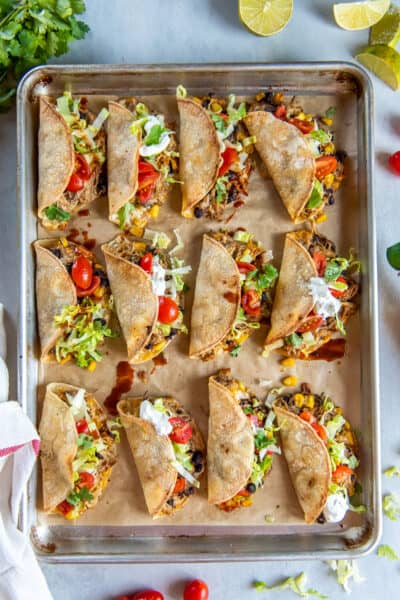 A sheet pan full of chicken tacos filled with lettuce, tomatoes, and sour cream.