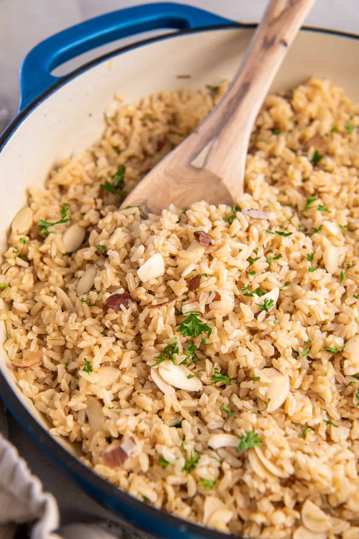 A wooden spoon scooping brown rice pilaf from a skillet.