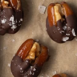 Chocolate dipped dates stuffed with walnuts on parchment paper.
