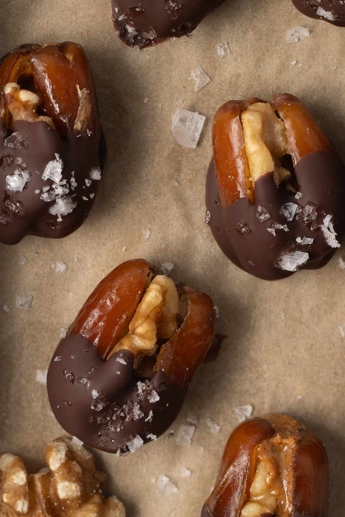 Chocolate dipped dates stuffed with walnuts on parchment paper.