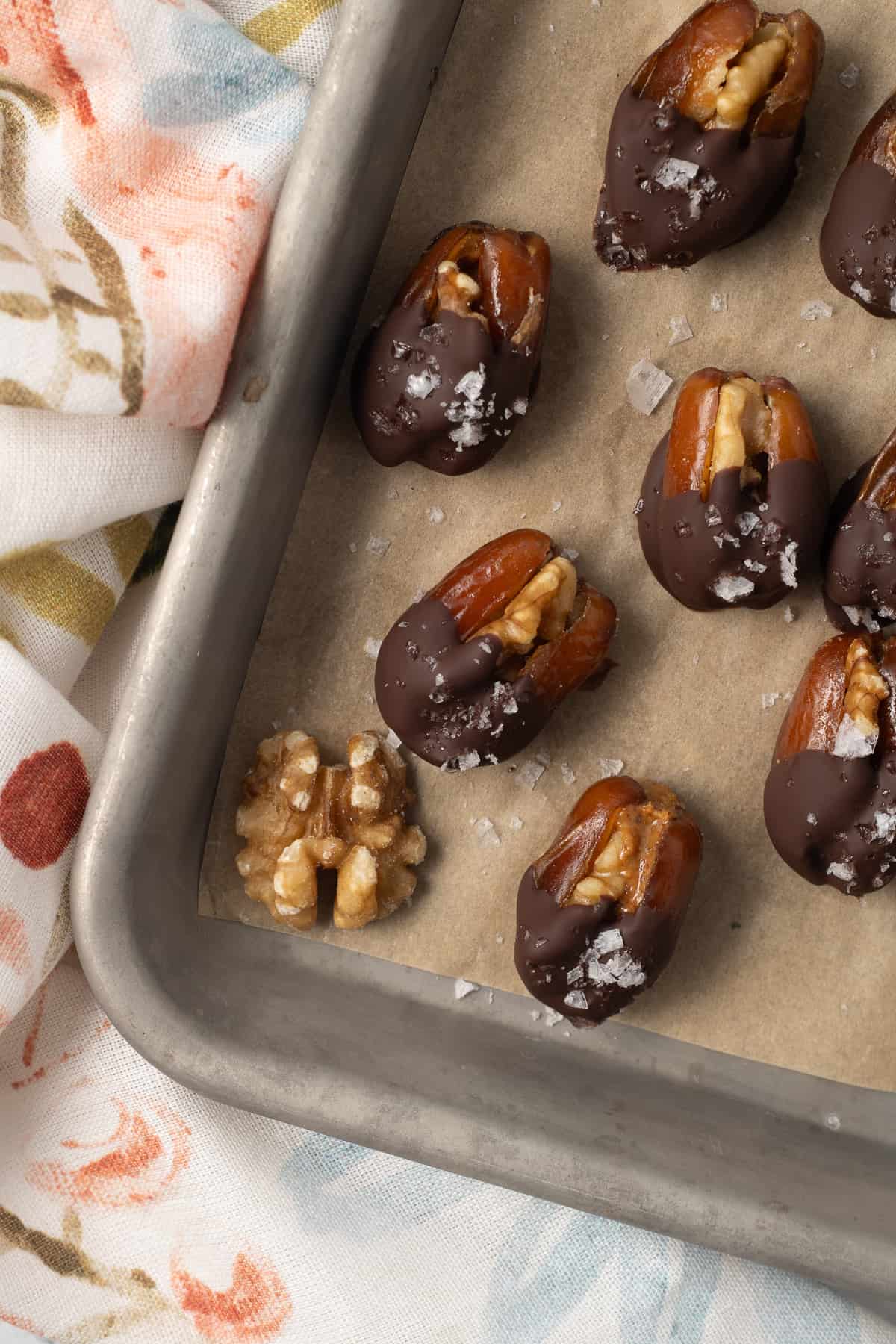 Chocolate dipped walnut stuffed dates on a baking sheet lined with parchment paper.