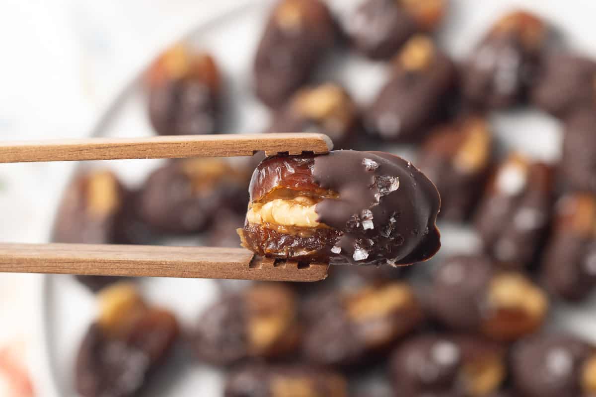Wooden tongs holding a chocolate dipped walnut stuffed date.