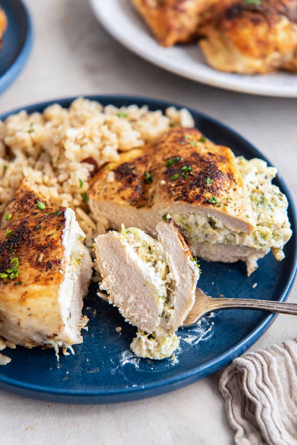 A piece of stuffed chicken cut in half on a blue plate with a fork.