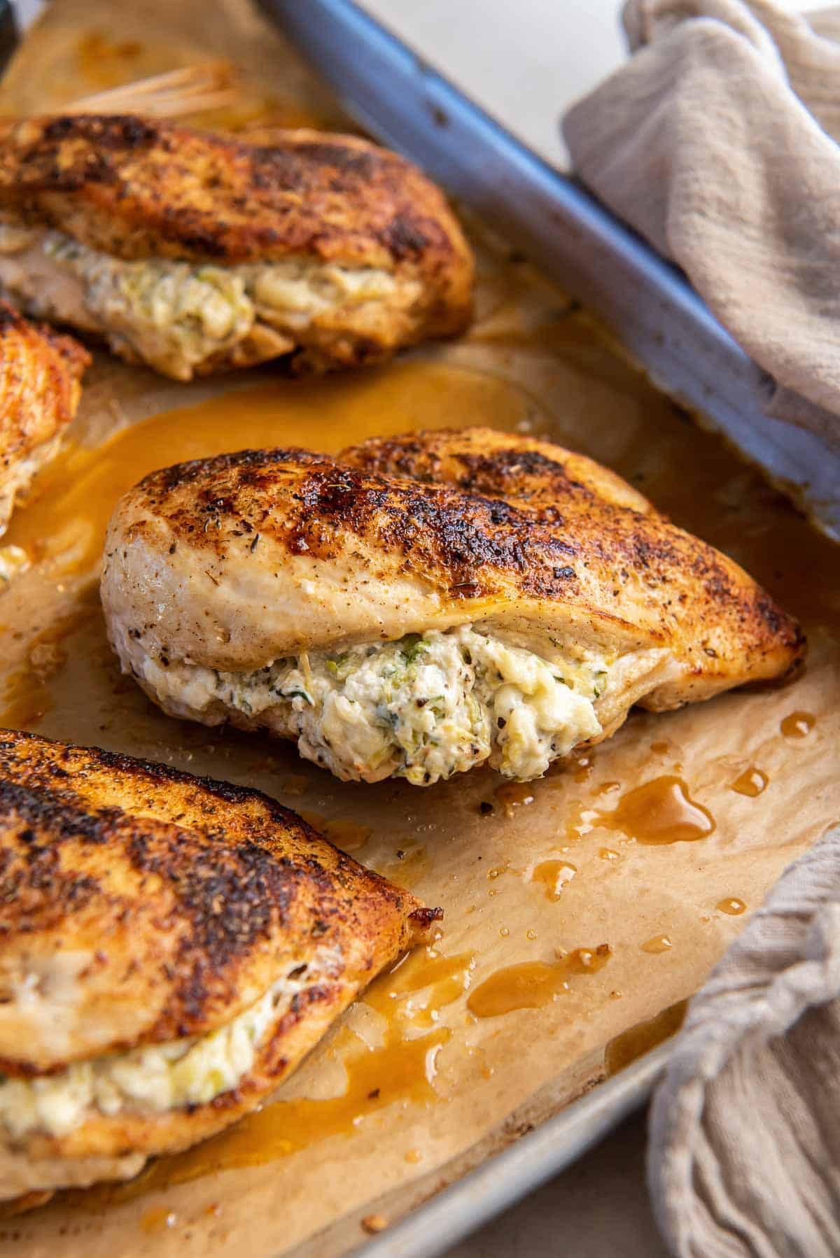 Four pieces of zucchini feta stuffed chicken on a baking sheet lined with parchment paper.